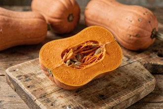 Butternut coupée en deux sur une planche en bois rustique, révélant la chair orange vive et les graines, idéale pour illustrer la densité calorique de ce légume